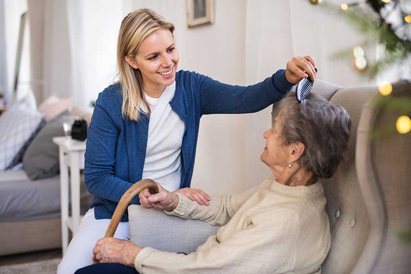 A health visitor combing hair of senior woman at home at Christmas time. A health visitor combing hair of senior woman at home at Christmas time.
