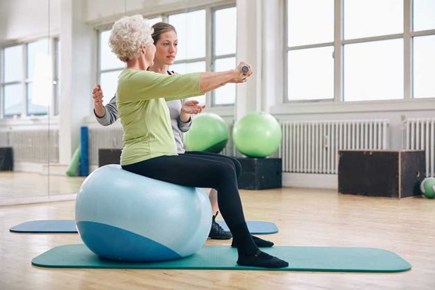 Female trainer assisting senior woman lifting weights Female trainer assisting senior woman lifting weights