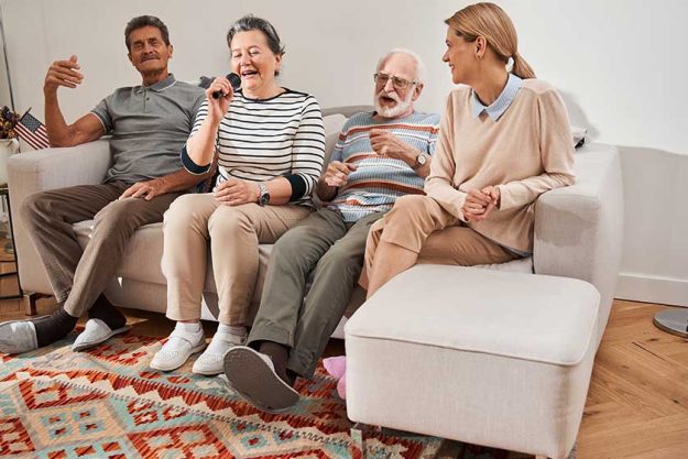 Group of senior people singing while sitting at the sofa with their caregiver Group of senior people singing while sitting at the sofa with their caregiver