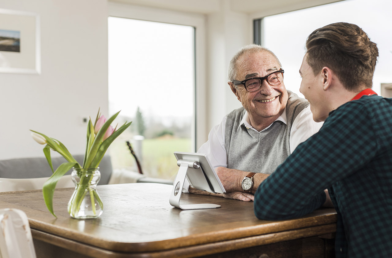 Happy senior man and his grandson sitting at table in the living room Everything You Need To Know About Taking Care Of Grandparents