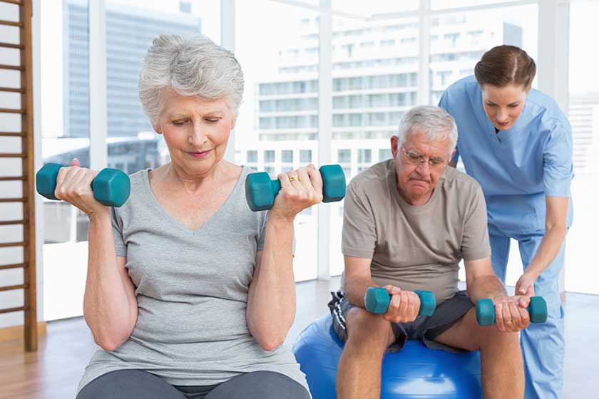 Female therapist assisting senior couple with dumbbells