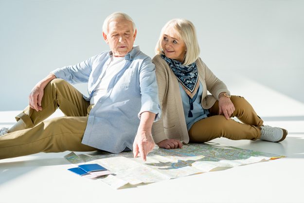 serious senior man pointing at traveling map with smiling wife