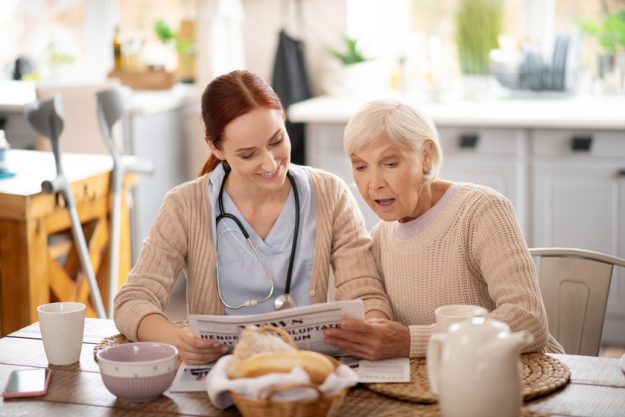 Caregiver reading morning news for retired woman Behavioral Care In Senior Apartments & Why It Is Important For Your Loved Ones