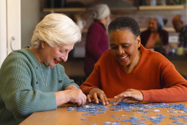 Happy diverse senior female friends playing with jigsaw Happy diverse senior female friends playing with jigsaw
