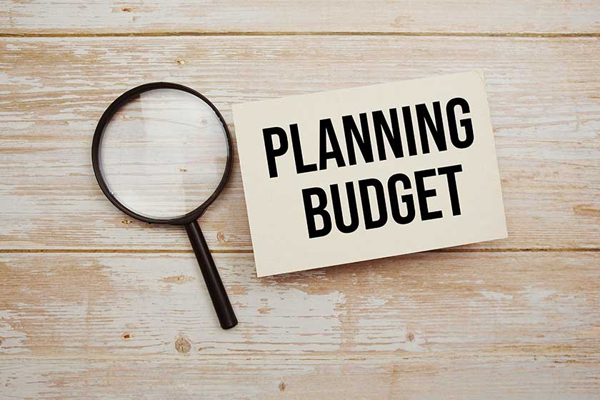 Planning Budget text message and magnifying glass with space copy on wooden background