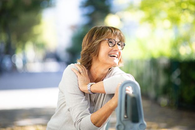 Close up portrait older woman sitting on park bench laughing