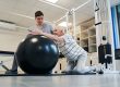 Pensioner standing on knees while putting arms on exercise ball
