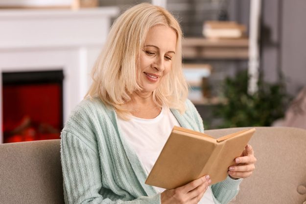 Beautiful mature woman reading book at home on autumn day