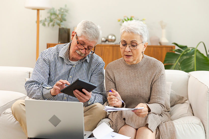 Middle aged senior couple sit with laptop and paper document. Older mature man woman reading paper bill pay online at home managing bank finances calculating taxes planning loan debt pension payment