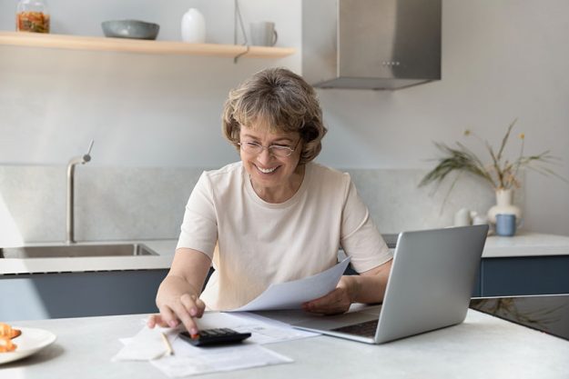 Smiling elderly senior retired woman calculating domestic expenditures.