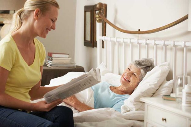 Daughter-Reading-Newspaper-To-Senior-Parent