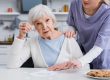 Elderly-woman-showing-piece-of-jigsaw-puzzle-while-nurse