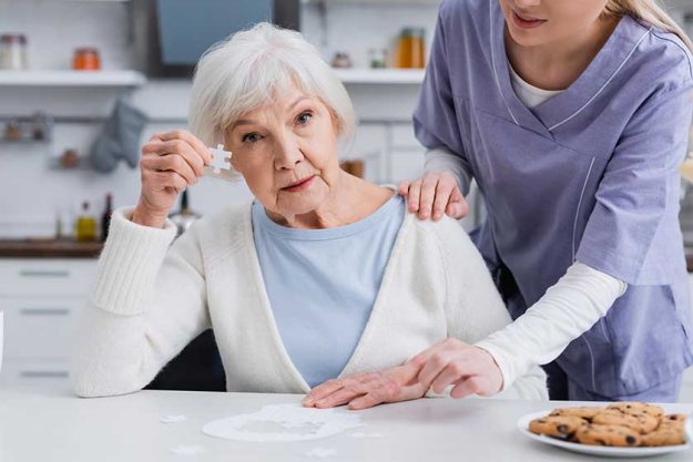 Elderly-woman-showing-piece-of-jigsaw-puzzle-while-nurse