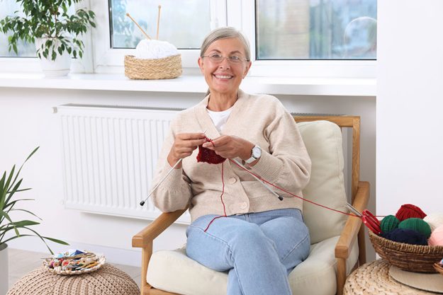Smiling senior woman knitting on armchair Smiling senior woman knitting on armchair