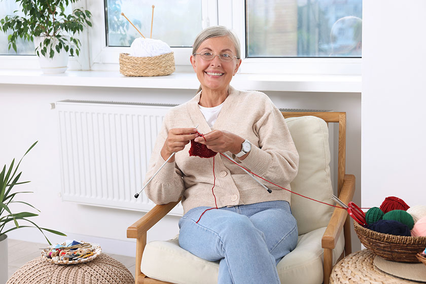 Smiling senior woman knitting on armchair