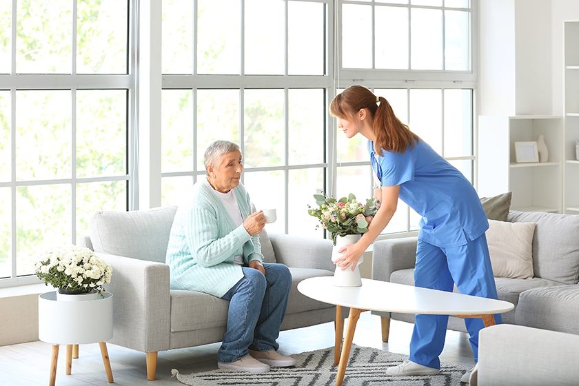 senior-woman-caregiver-putting-bouquet-flowers Senior woman and caregiver putting bouquet of flowers