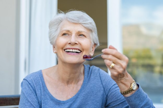 Cheerful,Senior,Woman,Holding,Red,Grapes,In,Spoon,And,Make
