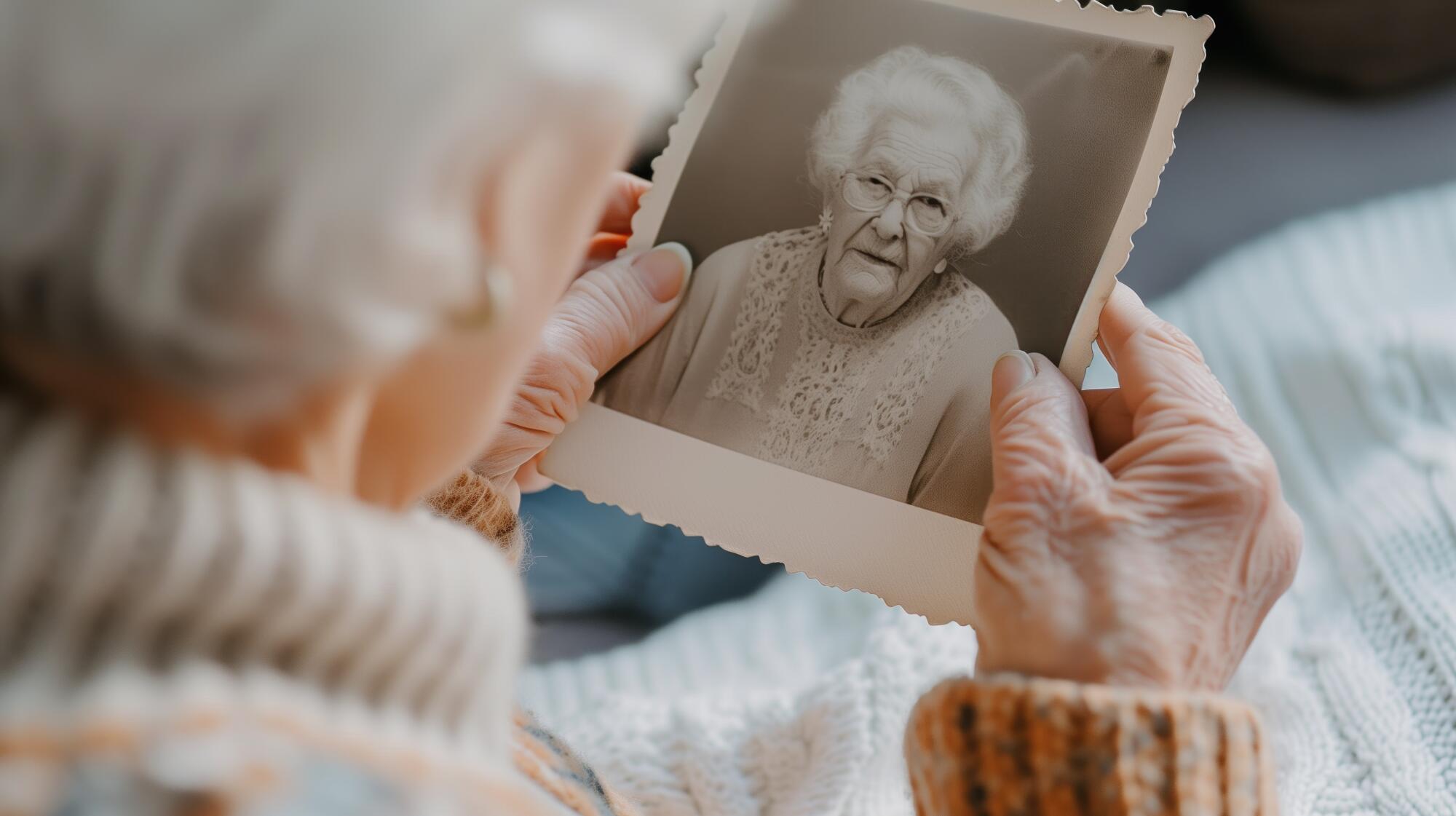 Elderly woman reflects on memories with vintage photograph. Themes of nostalgia and memory.